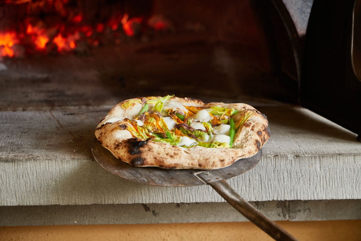 Pizza coming out of a wood-fired oven